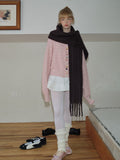 Woman wearing a pink knitted cardigan and a long dark brown scarf, looking towards the camera.
