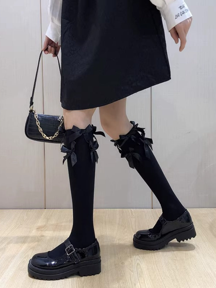 Model wearing black knee-high socks adorned with black bows, paired with a black skirt and Mary Jane shoes.