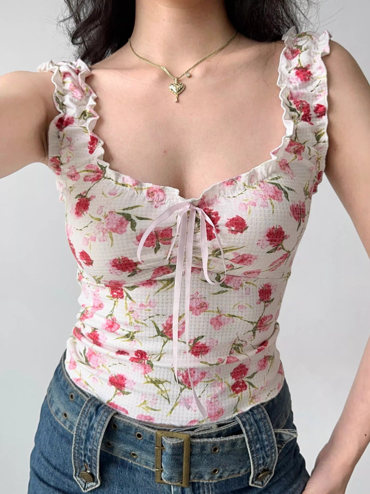 Front view of a woman wearing a white floral print top with ruffled off-the-shoulder cap sleeves and a sweetheart neckline with a pink ribbon tie.