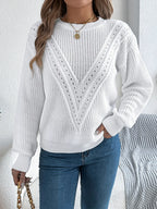 Woman holding a handbag while wearing a white long-sleeve knit sweater and blue jeans