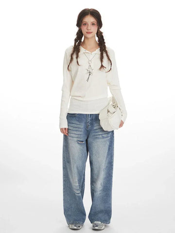 Woman wearing a white ribbed knit long-sleeve top with a collared button-up neckline and a detachable hood, paired with light-wash baggy jeans and a white handbag.
