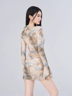 Rear view of a woman in a sheer abstract print two-piece set, showing the back of the top and the ruched skirt.