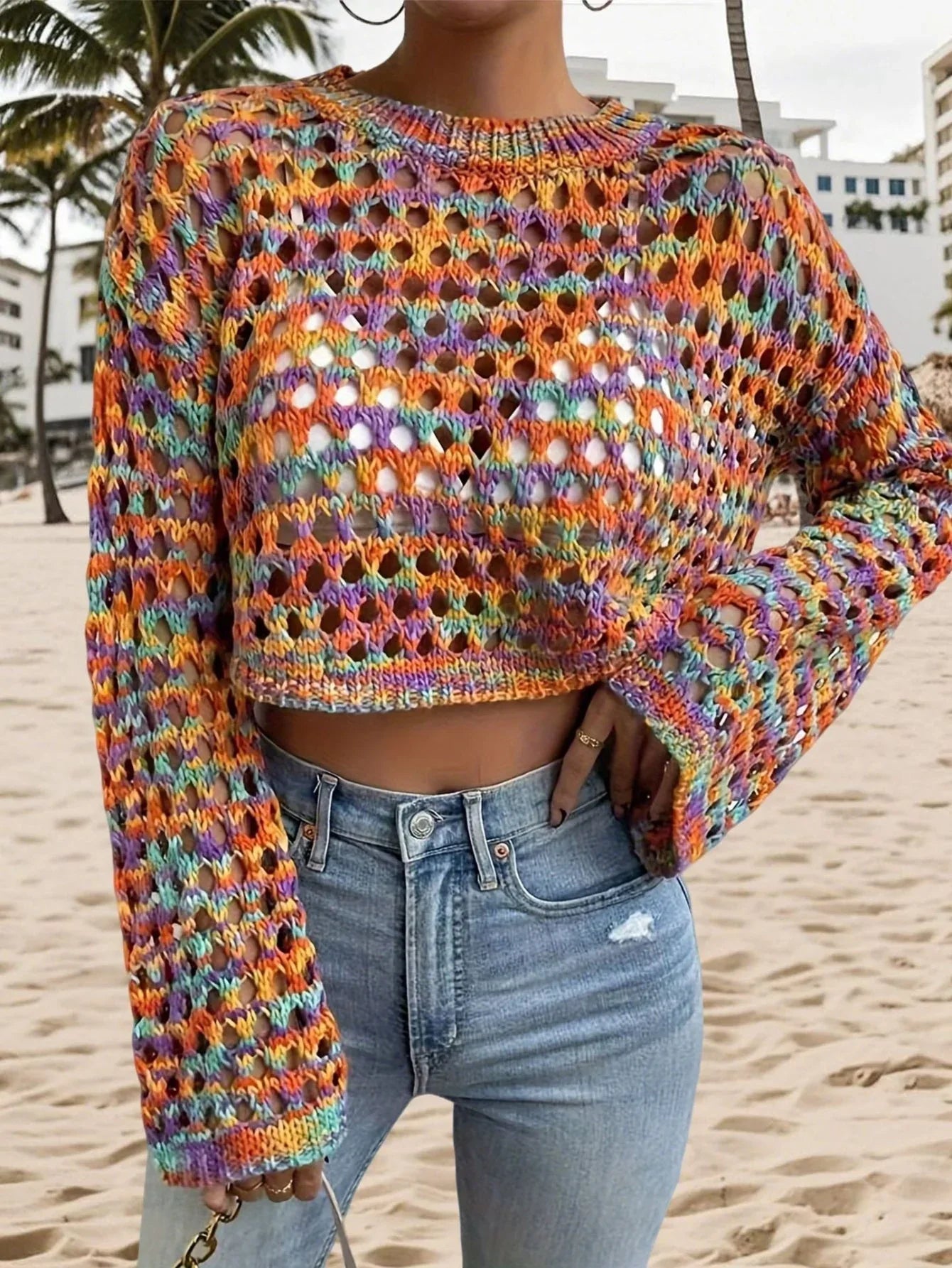 Front close-up of a woman wearing a multi-color cropped hollow-out knit sweater and light wash jeans