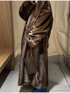 Side view of a woman wearing a long brown faux fur coat and blue jeans, holding a clutch.