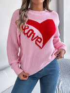 Close-up of the front of a pink knit sweater featuring a red heart and 'love' graphic.