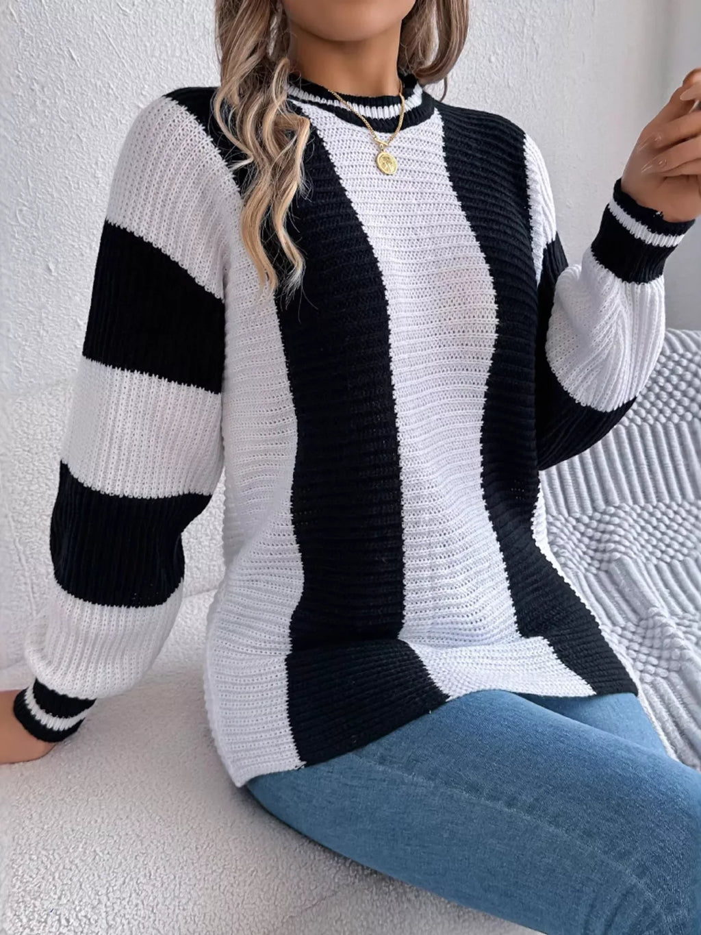 Woman sitting on a couch wearing a black and white striped knit sweater and blue jeans.