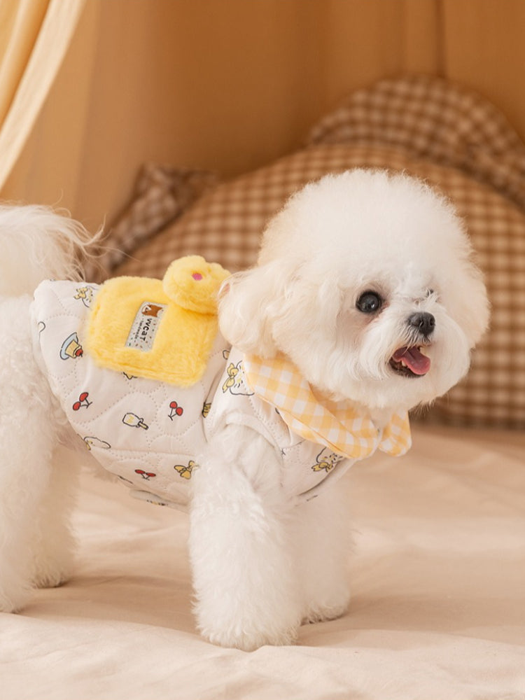 Side view of a white bichon frise dog wearing a white quilted vest with a yellow gingham collar and cartoon prints