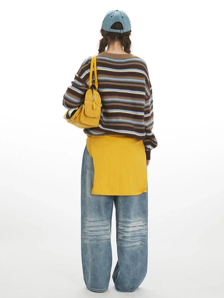 Woman wearing a brown, blue, and yellow striped knit sweater with a crew neck and long sleeves.