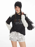 Front close-up of a model wearing a black and white long sleeve graphic t-shirt and silver ruffled shorts.