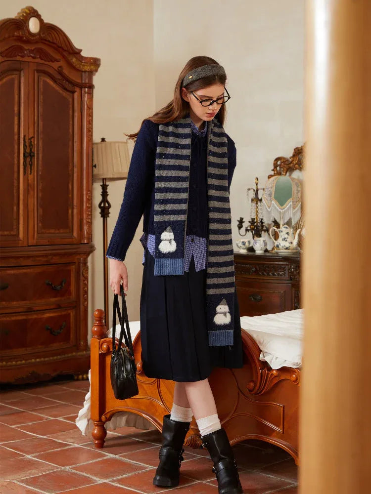 Woman wearing a navy knit sweater with gray and navy horizontal stripes and snowman embellishments on the scarf.