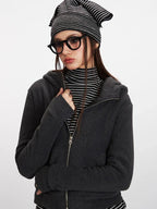 Woman wearing a charcoal grey zip-up hooded fleece jacket and striped turtleneck, adjusting her jacket.