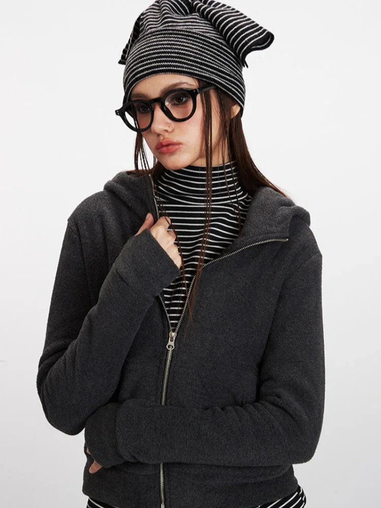 Woman wearing a charcoal grey zip-up hooded fleece jacket and striped turtleneck, adjusting her jacket.