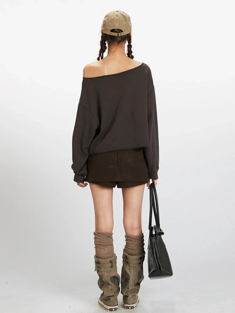 Woman wearing a dark grey distressed graphic print cropped sweatshirt with an off-the-shoulder neckline, paired with a dark brown mini skirt and knee-high socks with boots.
