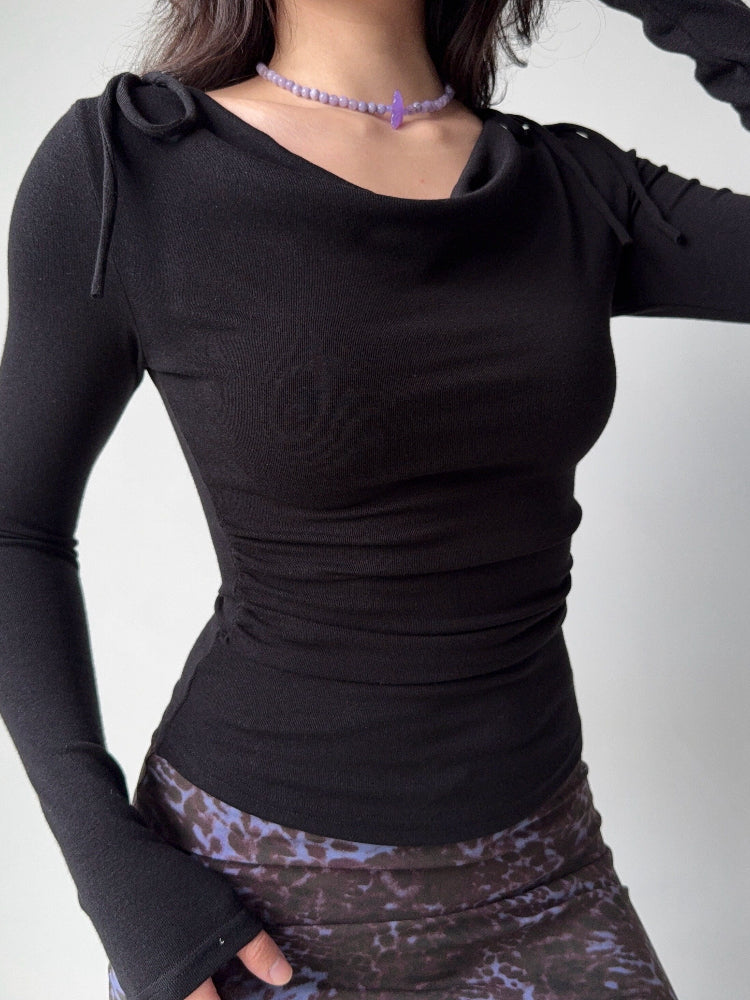 Woman wearing a black long-sleeve top with a drape neckline and tie shoulder details.