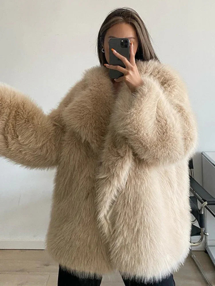 Full body shot of a woman wearing a brown shaggy faux fur coat, cream turtleneck, and blue jeans standing in front of a red door.