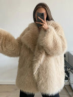 Full body shot of a woman wearing a brown shaggy faux fur coat, cream turtleneck, and blue jeans standing in front of a red door.