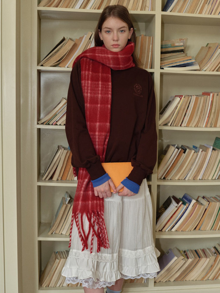 Woman in a white long-sleeved shirt with lace trim and a ruffled white skirt, wearing a grey plaid scarf.