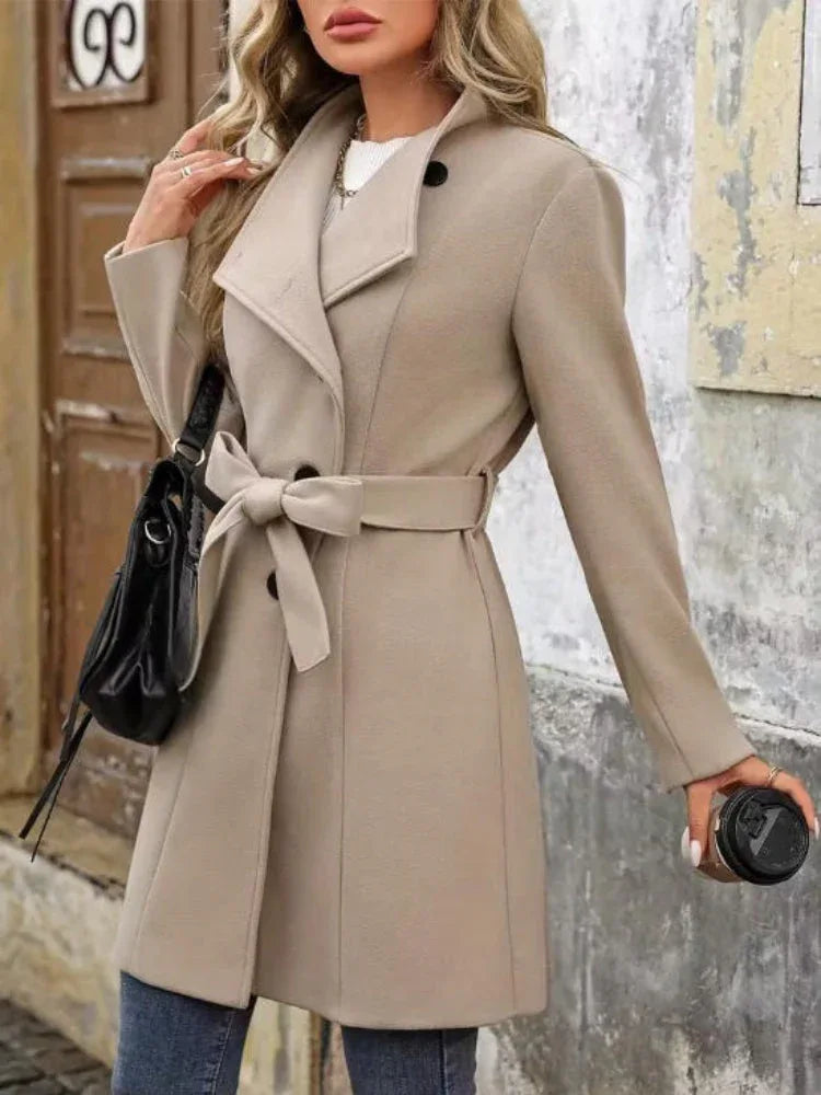 Woman holding a coffee cup and wearing a beige wool blend coat with belted waist and asymmetrical closure