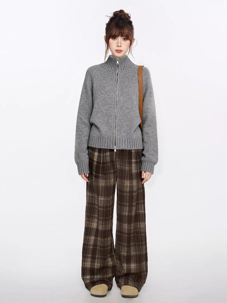 Full body shot of a woman in a grey knit zip-up sweater and brown plaid wide-leg pants