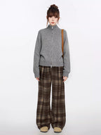 Full body shot of a woman in a grey knit zip-up sweater and brown plaid wide-leg pants