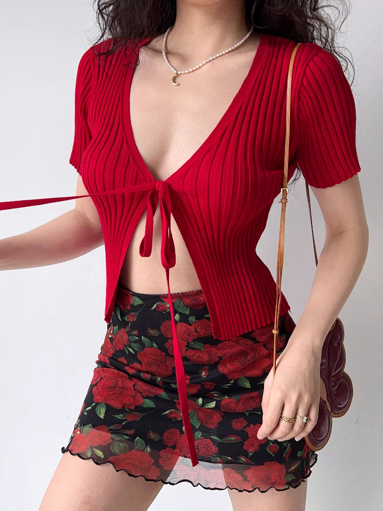 Detail of the tie front closure on a red ribbed knit cropped cardigan.