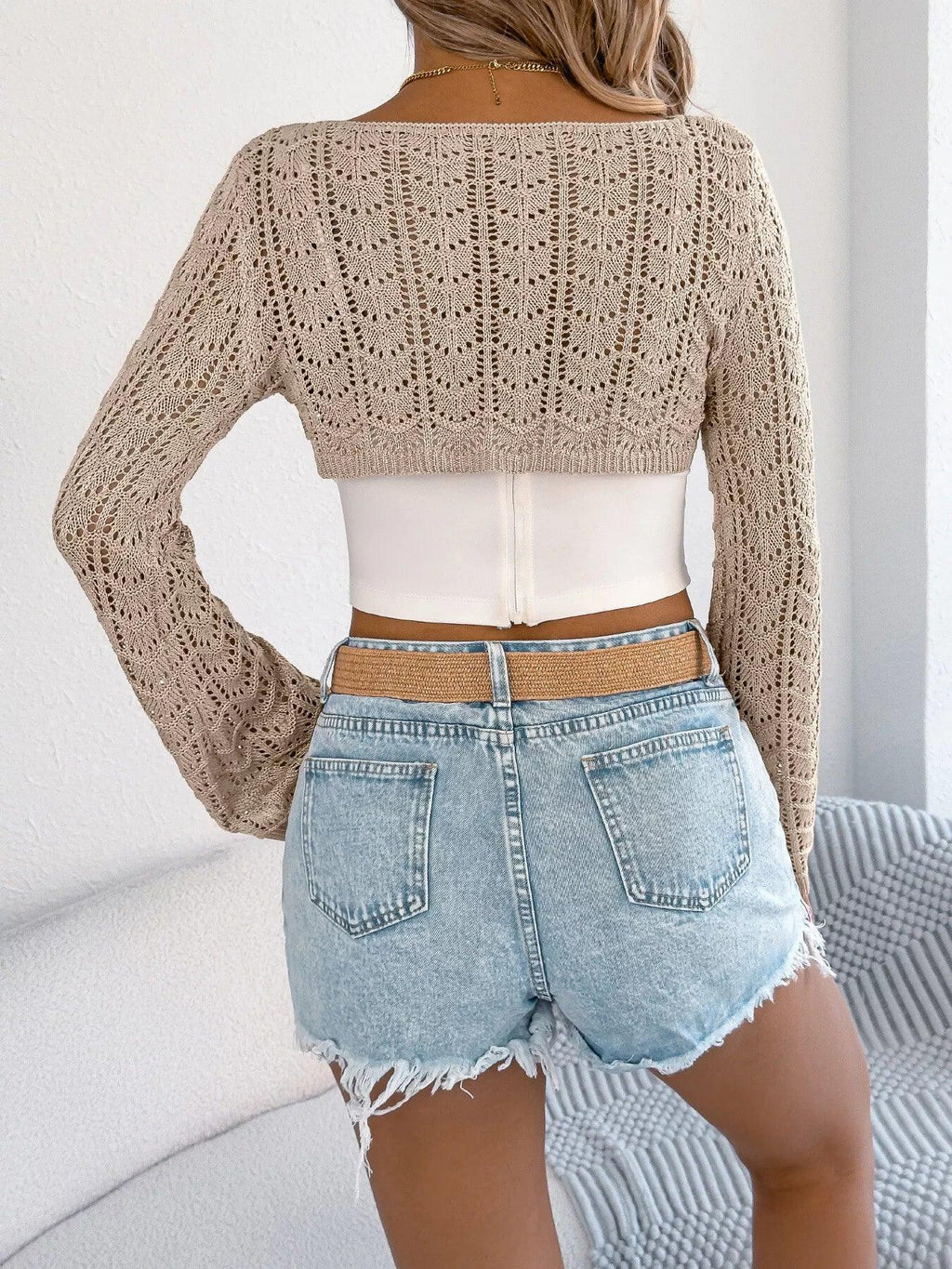 Back view of a woman wearing a beige open-knit bolero over a white camisole.