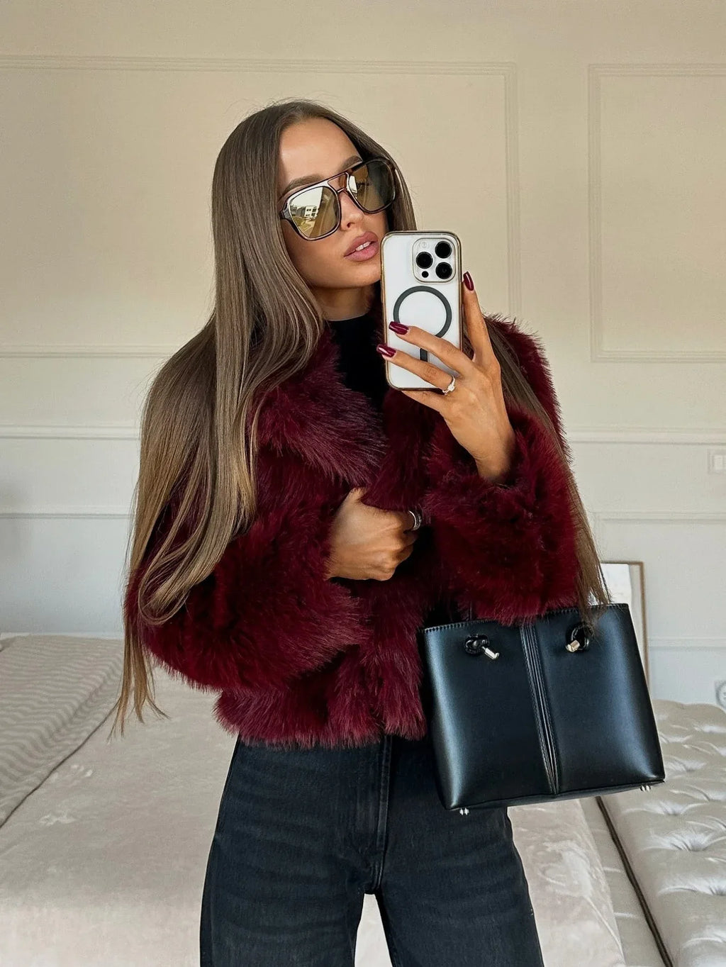 Woman wearing a burgundy faux fur jacket and black jeans, holding a black handbag.