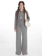 Woman wearing a grey ribbed knit loungewear set with a full zip jacket and wide leg pants, carrying a white shoulder bag.