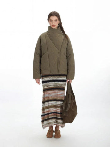Woman wearing a quilted olive green jacket with an asymmetrical high neck and long sleeves.