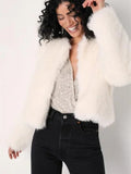 Woman smiling, wearing a white faux fur cropped jacket over a sparkly top and black jeans.