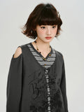 Close-up of a woman wearing a dark gray graphic print cropped long-sleeve top with cold shoulder cutouts and a lace-up front over a gray and white striped t-shirt, accessorized with a beaded necklace.