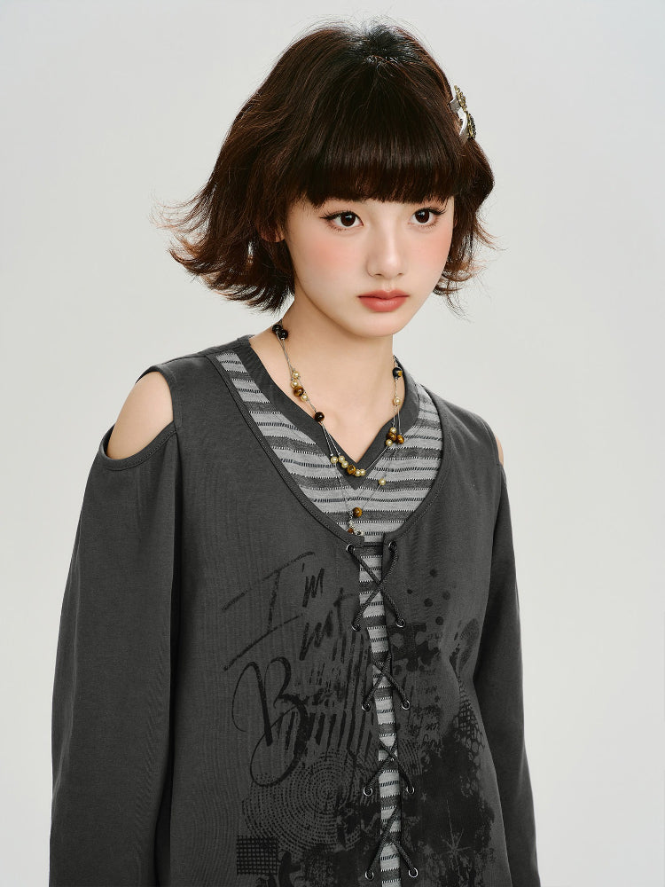 Close-up of a woman wearing a dark gray graphic print cropped long-sleeve top with cold shoulder cutouts and a lace-up front over a gray and white striped t-shirt, accessorized with a beaded necklace.