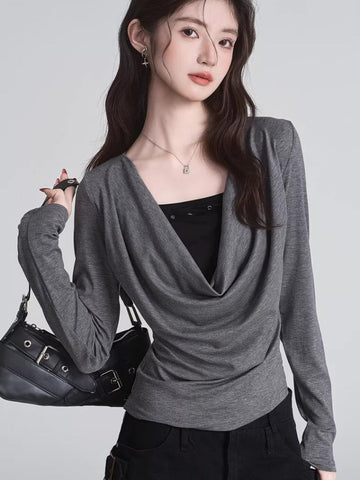 Woman wearing a grey long-sleeve draped cowl neck top over a black camisole, holding a black handbag.
