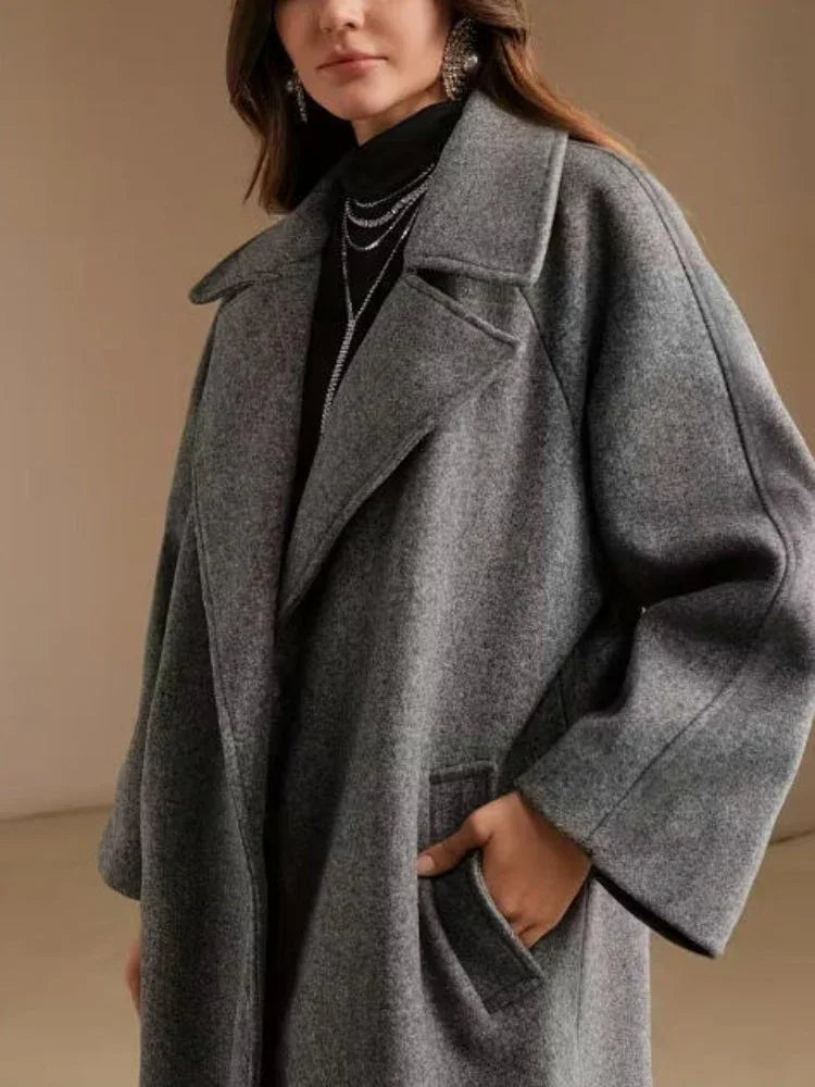 Close-up of a woman's grey wool blend coat, showcasing the lapel and side pocket detail.