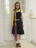 Full body shot of a woman wearing a yellow long-sleeve shirt, navy camisole, denim skirt, white socks, brown shoes, and a multi-colored striped fuzzy scarf.