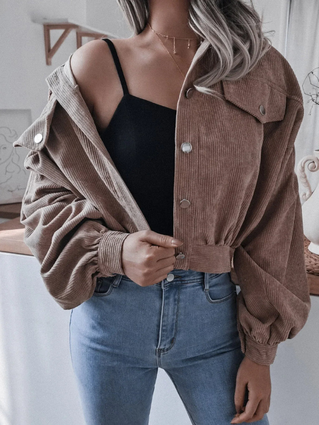 Woman wearing a brown corduroy cropped jacket, open at the front, revealing a black crop top and blue jeans.