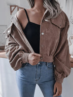 Woman wearing a brown corduroy cropped jacket, open at the front, revealing a black crop top and blue jeans.