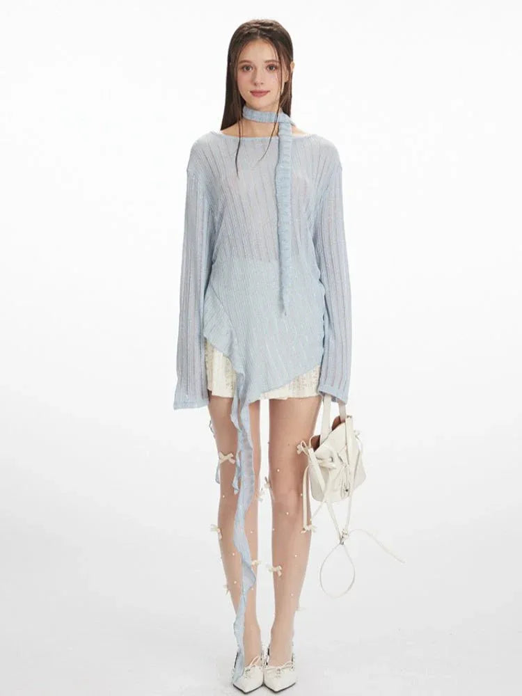 Woman wearing a light blue shimmering knit long-sleeve top with a scarf tie and asymmetrical hem