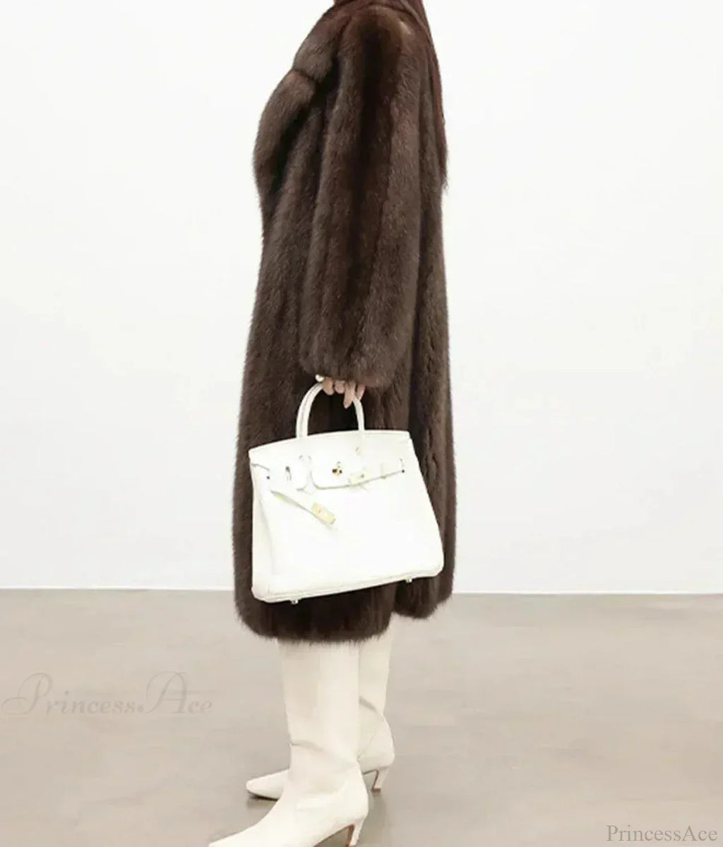 Side view of a woman in a brown mink fur coat holding a white handbag.