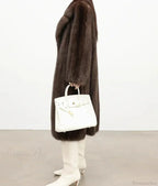 Side view of a woman in a brown mink fur coat holding a white handbag.