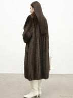 Rear view of a woman wearing a long brown mink fur coat and white boots.