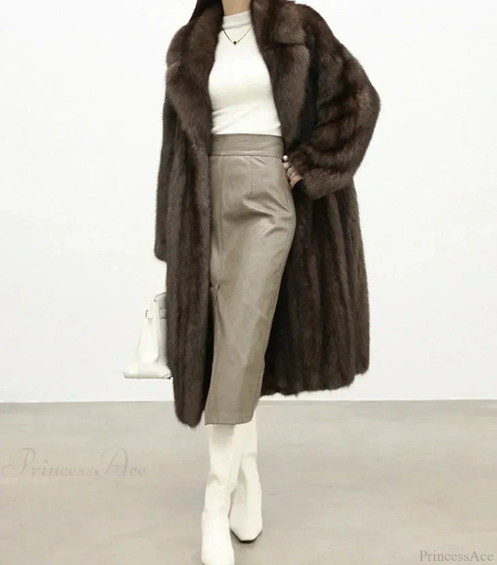 Woman wearing a full-length brown mink fur coat with a notched collar and white turtleneck, paired with a grey leather pencil skirt and white boots.