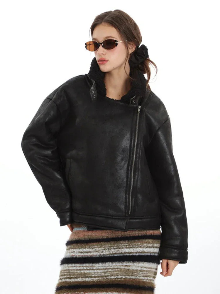 Woman wearing a black faux leather aviator jacket with shearling collar and lapel details, styled with sunglasses.