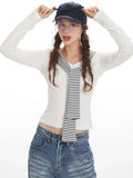 Woman in a white long-sleeve top with a striped collar and blue wide-leg jeans, adjusting her baseball cap.