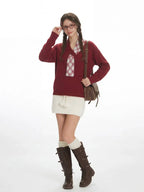 Full-length studio shot of a woman in a burgundy V-neck sweater and white skirt.