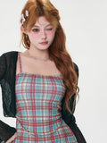 Close-up of a woman's torso wearing a black sheer bell sleeve cardigan and a red and blue plaid spaghetti strap mini dress.