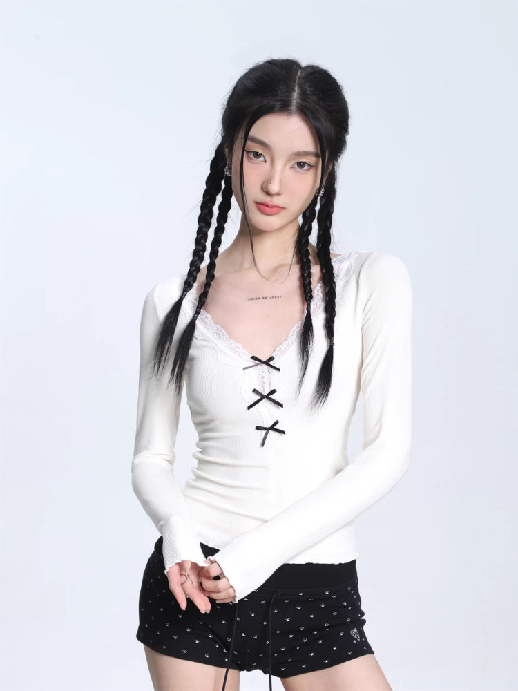 Woman wearing a white long-sleeve ribbed knit top with a V-necklace and lace trim, featuring a decorative bow and lace-up front detail.