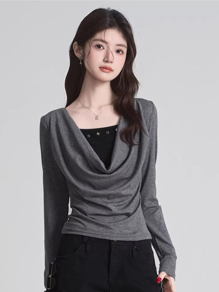 Woman wearing a grey long-sleeve draped cowl neck top over a black camisole, holding a black handbag.