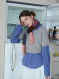 Young woman leaning against a refrigerator, styled in a casual layered outfit with a patterned scarf.