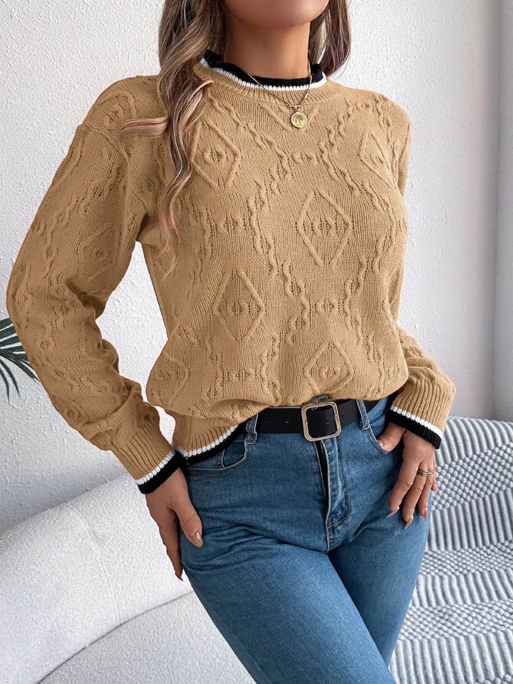 Front view of a woman in a tan geometric pattern sweater with blue jeans.